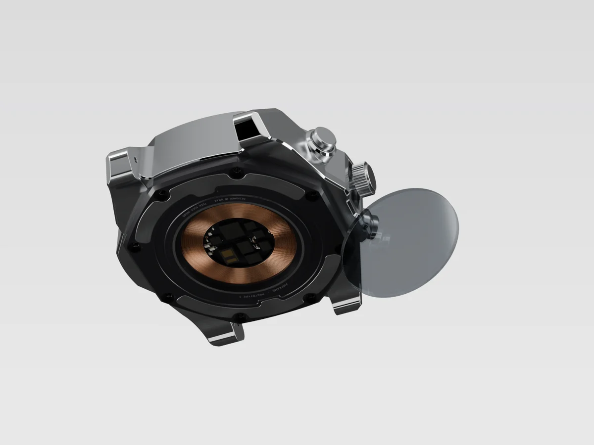 Render of the watch from below with the round caseback window lifted out beside it, the charging coil and sensors behind the opening.